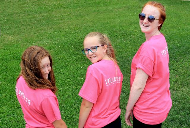 Three smiling young women wearing pink t-shirts with "volunteer" written on them